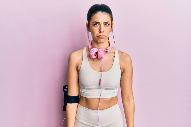 Young hispanic woman wearing gym clothes and using headphones depressed and worry for distress, crying angry and afraid. sad expression.  - Photo, Image