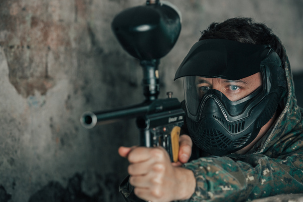 Paintball aksiyon oyununda maskeli ve silahlı genç bir adamın portresi, birbirlerine boya kapsülleri atmak için hava tabancaları kullanarak askeri savaş simülasyonu. - Fotoğraf, Görsel
