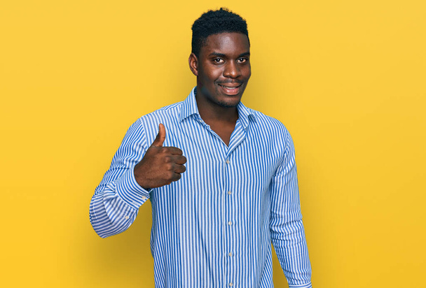 Knappe business zwarte man dragen casual gestreepte t-shirt glimlachen gelukkig en positief, duim omhoog doen uitstekend en goedkeuring teken  - Foto, afbeelding