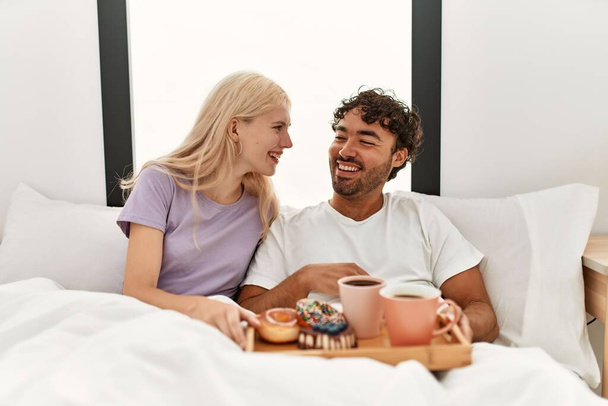 Νεαρό όμορφο ζευγάρι χαμογελά ευτυχισμένη έχοντας πρωινό στο κρεβάτι στο σπίτι. - Φωτογραφία, εικόνα