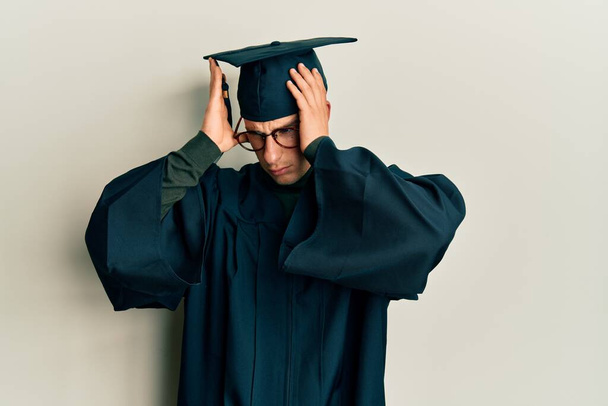 Young caucasian man wearing graduation cap and ceremony robe suffering from headache desperate and stressed because pain and migraine. hands on head.  - Photo, Image