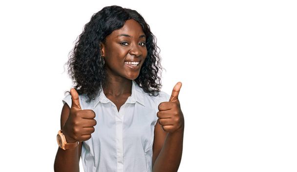 Beautiful african young woman wearing casual clothes success sign doing positive gesture with hand, thumbs up smiling and happy. cheerful expression and winner gesture.  - Фото, изображение