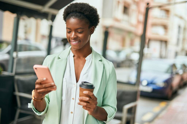 Młoda afrykańska bizneswoman używa smartfona pijącego kawę w mieście. - Zdjęcie, obraz