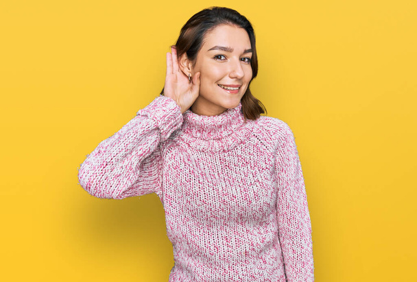 Fiatal kaukázusi lány gyapjú téli pulóvert visel, fültől fülig mosolyog, hallgatja a pletykát vagy pletykát. süketség fogalma.  - Fotó, kép