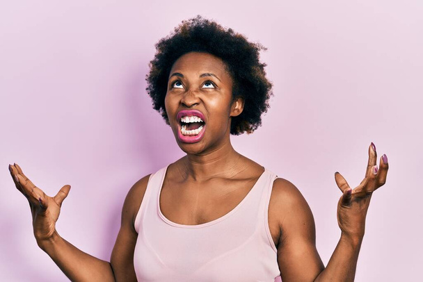 Mladá Afroameričanka v tričku bez rukávů šíleně a šíleně křičela a křičela s agresivním výrazem a zdviženýma rukama. koncepce frustrace.  - Fotografie, Obrázek
