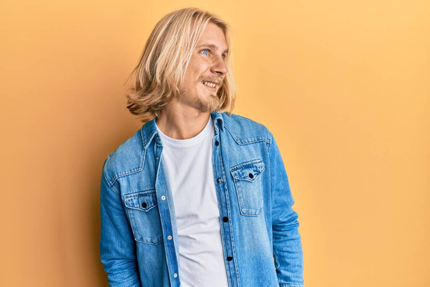 Caucasian man with blond long hair wearing casual denim jacket looking to side, relax profile pose with natural face and confident smile.  - Foto, Imagen