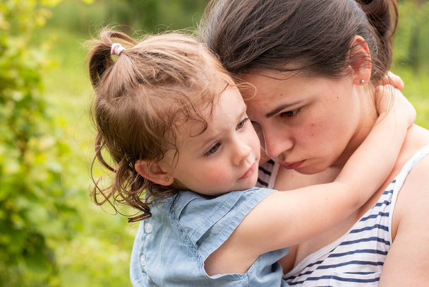 Malá dívka v džínové šaty v náručí její smutné maminky - Fotografie, Obrázek