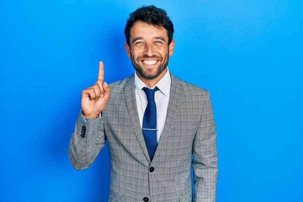 Bello uomo con la barba indossa abito da lavoro e cravatta mostrando e indicando con il dito numero uno, mentre sorridente fiducioso e felice.  - Foto, immagini