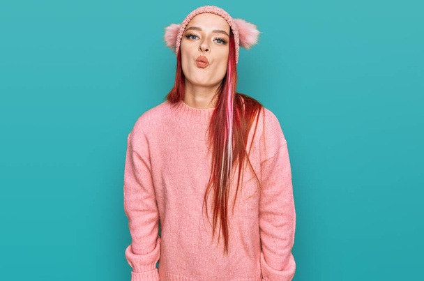 Jeune femme caucasienne portant des vêtements décontractés et bonnet de laine gonflant les joues avec un visage drôle. bouche gonflée d'air, expression folle.  - Photo, image