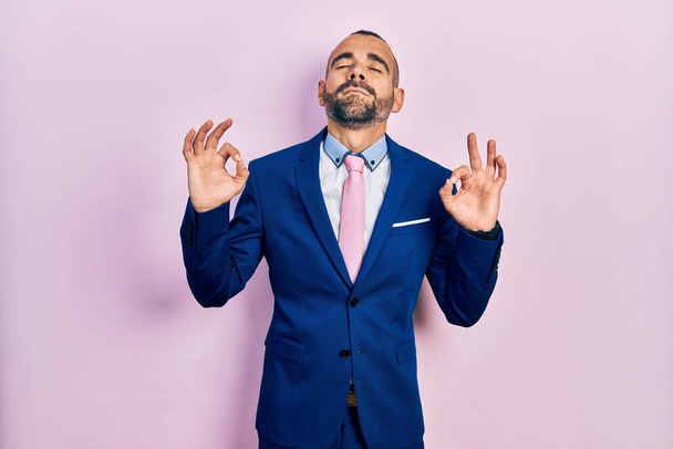 Young hispanic man wearing business suit and tie relaxed and smiling with eyes closed doing meditation gesture with fingers. yoga concept.  - Photo, image