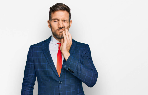 Handsome man with beard wearing business suit and tie touching mouth with hand with painful expression because of toothache or dental illness on teeth. dentist  - Photo, Image