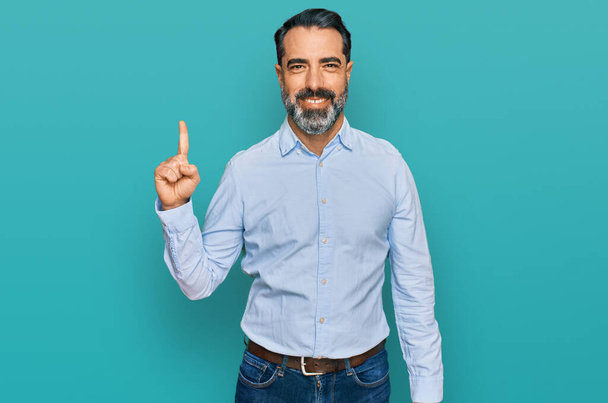 Middle aged man with beard wearing business shirt showing and pointing up with finger number one while smiling confident and happy.  - Photo, Image