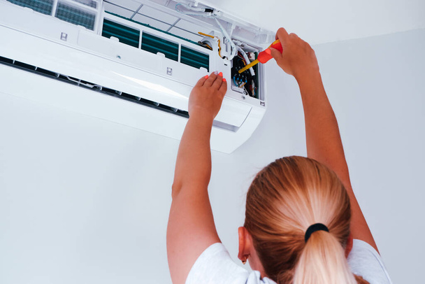 Reparatur der Klimaanlage. Eine Frau mit einem Schraubenzieher in der Hand repariert eine Klimaanlage. - Foto, Bild