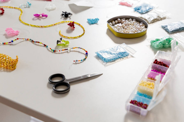 Creative, bright and colorful beads on the white table. Handicraft workplace. Beautiful diy jewelry and calming stress relieving hobby and activity - Фото, зображення