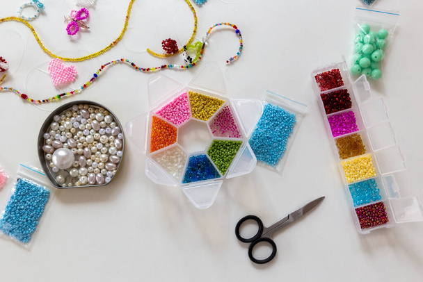 Creative, bright and colorful beads on the white table. Handicraft workplace. Beautiful diy jewelry and calming stress relieving hobby and activity - Photo, image