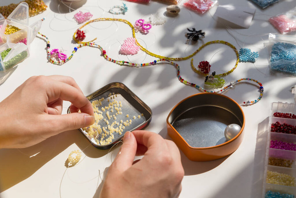 Beading workplace with hands in the process of handicraft. Beautiful diy jewelry and calming stress releasing hobby and activity - Photo, image