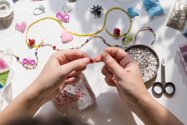 Beading workplace with hands in the process of handicraft. Beautiful diy jewelry and calming stress releasing hobby and activity - 写真・画像