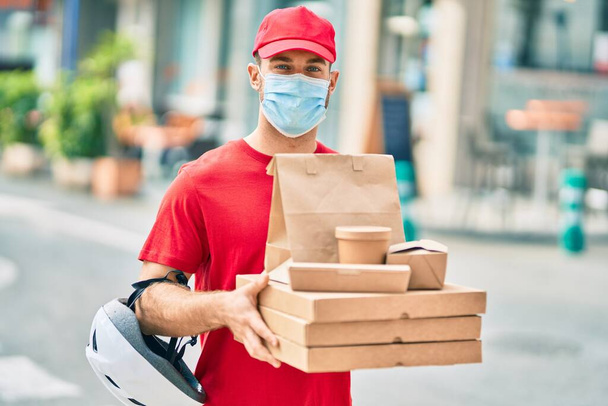 Jeune livreur caucasien portant un masque médical tenant la nourriture de livraison à la ville. - Photo, image
