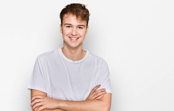 Young caucasian man wearing casual white t shirt happy face smiling with crossed arms looking at the camera. positive person.  - Foto, Bild