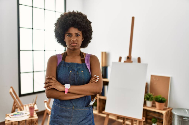 Mladá Afroameričanka s afro vlasy v ateliéru umění skeptická a nervózní, nesouhlasící výraz na tváři se zkříženýma rukama. negativní osoba.  - Fotografie, Obrázek