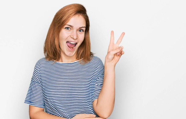 Young caucasian woman wearing casual clothes smiling with happy face winking at the camera doing victory sign. number two.  - Photo, Image