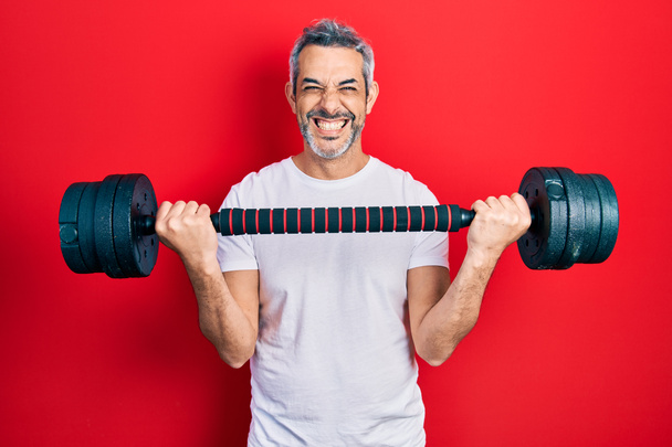 Handsome middle age man with grey hair wearing sportswear using dumbbells smiling with a happy and cool smile on face. showing teeth.  - Fotografie, Obrázek