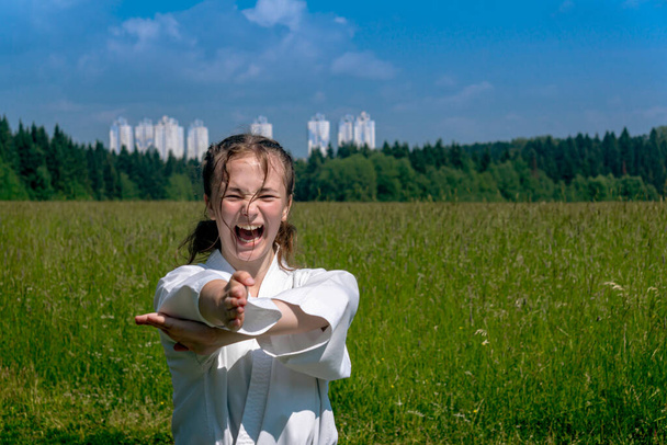 teenage girl practicing karate kata outdoors, performs nukite tsuki strike with kiai scream - Photo, image