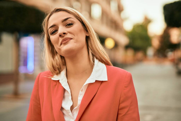 Młoda blondynka bizneswoman uśmiechnięta szczęśliwy stojąc w mieście. - Zdjęcie, obraz