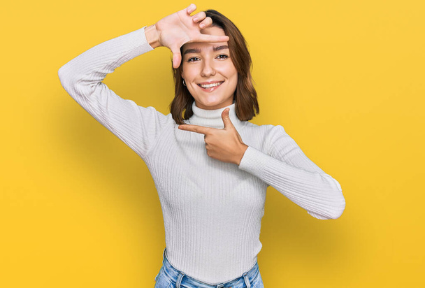 Young caucasian girl wearing casual clothes smiling making frame with hands and fingers with happy face. creativity and photography concept.  - Foto, afbeelding