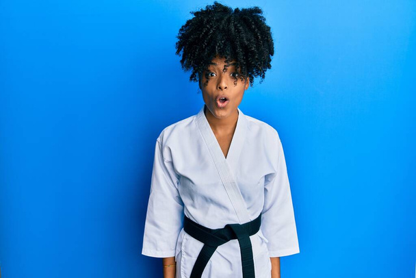 Afrikai amerikai nő afro haj visel karate kimono és fekete öv fél, és megdöbbent a meglepetés kifejezés, félelem és izgatott arc.  - Fotó, kép