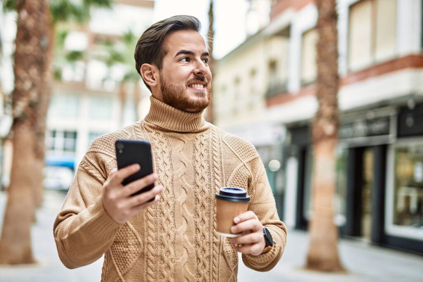Jonge Kaukasische man met smartphone die koffie drinkt in de stad. - Foto, afbeelding