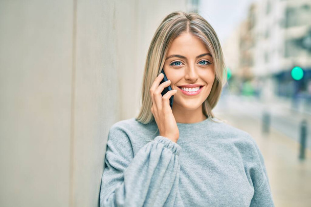 Jeune fille blonde souriante heureuse de parler sur le smartphone de la ville - Photo, image