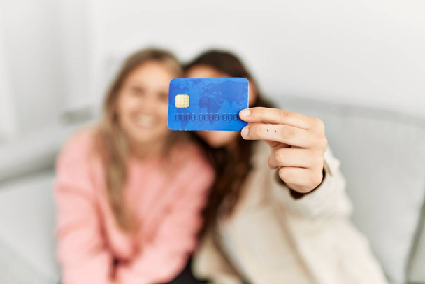 Joven pareja sonriendo feliz celebración de la tarjeta de crédito en casa. - Foto, imagen