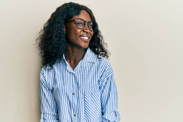 Hermosa mujer joven africana con ropa casual y gafas mirando al costado, pose de perfil relajado con rostro natural y sonrisa confiada.  - Foto, imagen
