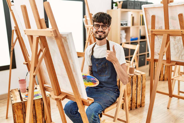 Sanat stüdyosunda sakallı, mutlu ve pozitif gülümseyen, mükemmel ve onay işareti yapan İspanyol bir adam.  - Fotoğraf, Görsel