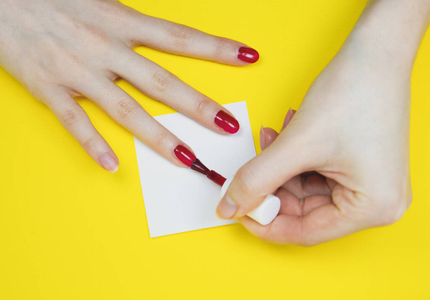 Женщина наносит красный лак на желтый фон - Фото, изображение