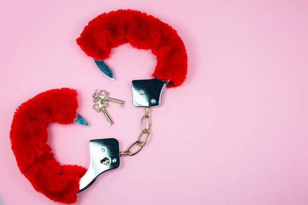Красные сексуальные пушистые наручники с ключами на розовом фоне. - Фото, изображение