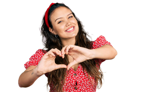 Nuori latino tyttö yllään rento vaatteita hymyillen rakastunut tekee sydän symboli muoto käsin. romanttinen käsite.  - Valokuva, kuva