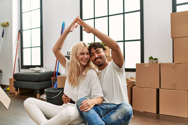 Young beautiful couple doing house symbol with arms raised at new home. - Fotoğraf, Görsel