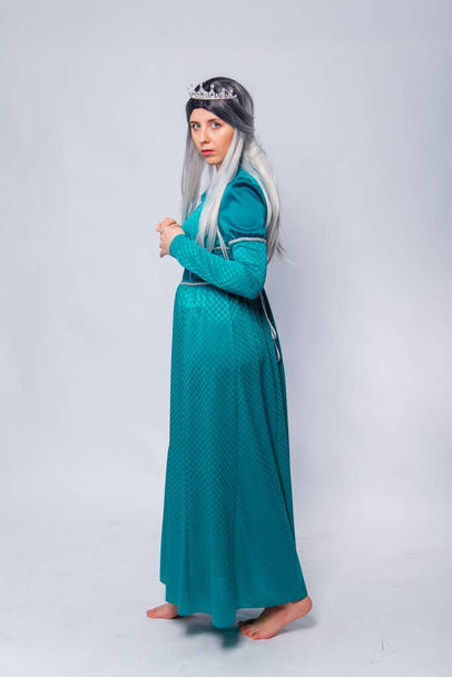 Full length portrait of a standing back princess in a medieval, fantasy, turquoise dress with ash hair and a silver crown posing isolated on a white background. - Foto, Bild