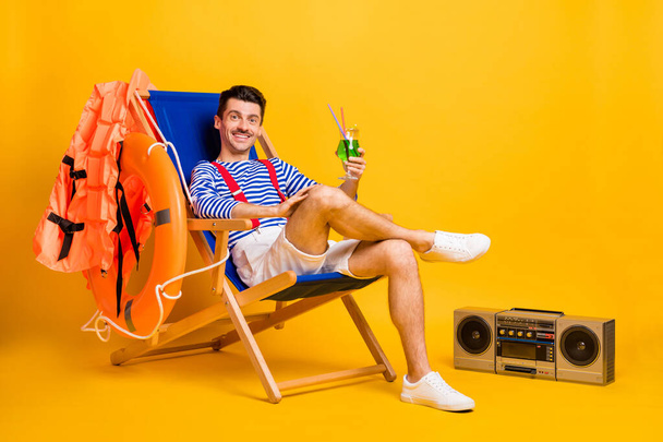 Full size photo of brown haired man hold cocktail sit chair beach lifeguard wear sailor outfit isolated on yellow color background - Φωτογραφία, εικόνα