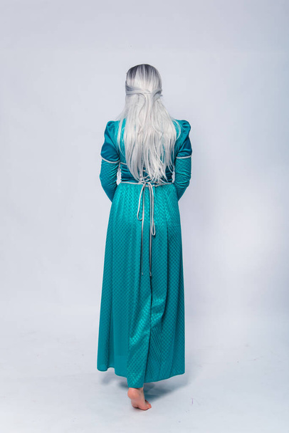 Full length portrait of a standing back princess in a medieval, fantasy, turquoise dress with ash hair and a silver crown posing isolated on a white background. - Foto, imagen