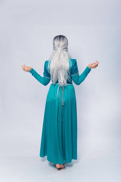 Full length portrait of a standing back princess in a medieval, fantasy, turquoise dress with ash hair and a silver crown posing isolated on a white background. - Photo, Image