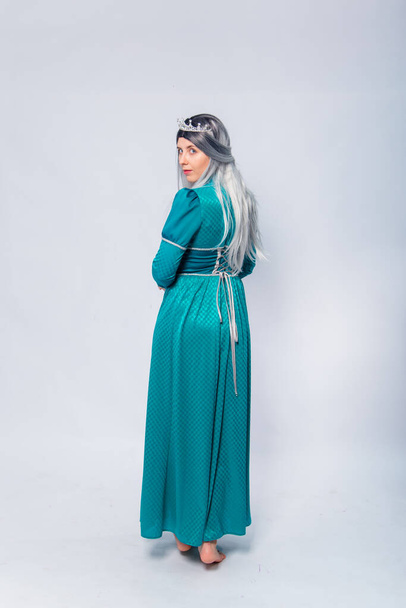 Full length portrait of a standing back princess in a medieval, fantasy, turquoise dress with ash hair and a silver crown posing isolated on a white background. - Fotografie, Obrázek