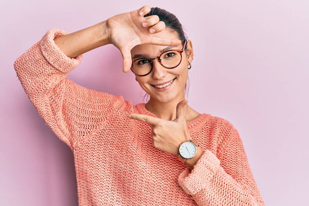 Young caucasian woman wearing casual clothes and glasses smiling making frame with hands and fingers with happy face. creativity and photography concept.  - Foto, Imagem