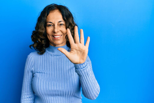 Mujer hispana de mediana edad vistiendo ropa casual mostrando y señalando con los dedos el número cinco mientras sonríe confiada y feliz.  - Foto, Imagen