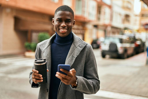 Young african american man using smartphone drinking coffee at the city - 写真・画像