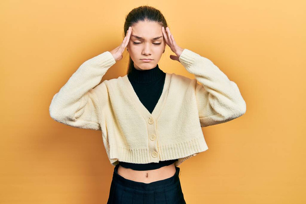 Jong brunette meisje draagt casual gele jas met de hand op het hoofd, hoofdpijn omdat stress. lijden aan migraine.  - Foto, afbeelding