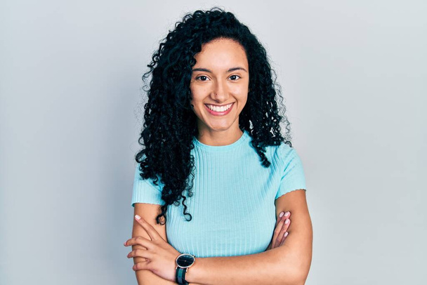 Young hispanic woman with curly hair wearing casual blue t shirt happy face smiling with crossed arms looking at the camera. positive person.  - Photo, Image