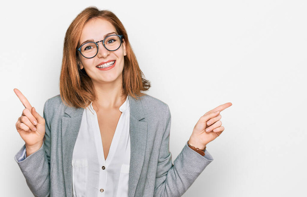 Молодая белая женщина в деловом стиле и в очках, уверенно улыбающаяся, указывая пальцами в разные стороны. копировальное место для рекламы  - Фото, изображение